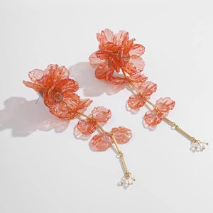 Détail des boucles d'oreilles pendantes en résine orange avec des accents en métal doré