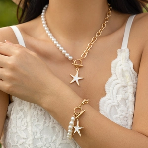 Dettaglio della collana asimmetrica con stella marina, perle e catena dorata su modella