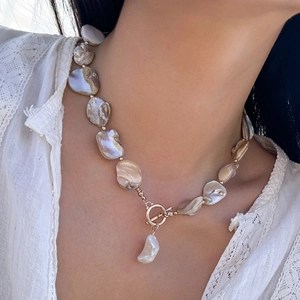 Dettaglio ravvicinato della collana di perle barocche con chiusura a T su pizzo bianco