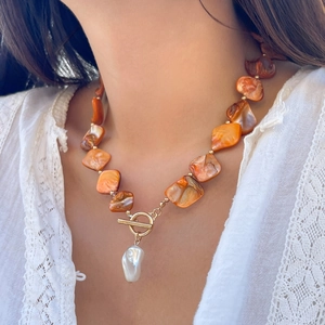 Dettaglio della collana boho con conchiglie arancioni, perla barocca e chiusura OT dorata