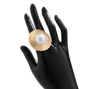 Detail eines Goldrings mit Faltenstruktur und großer weißer Kunstperle auf der Hand