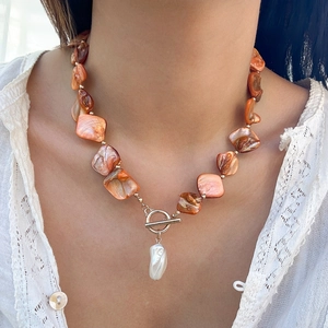 Dettaglio collana boho con perline di conchiglia, chiusura OT e perla barocca su modella