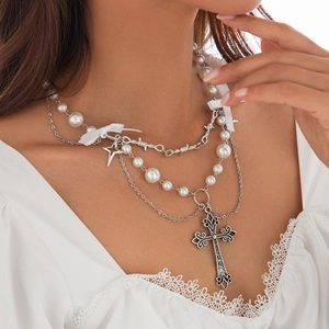 Dettaglio della collana con croce gotica, perle, catene metalliche e fiocco di seta bianco