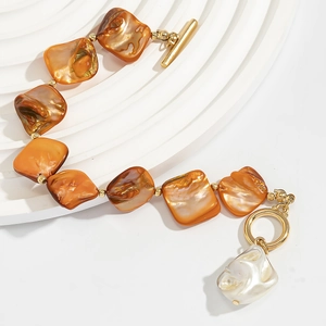 Dettaglio del bracciale con perle d'ambra, chiusura a T dorata e perla barocca bianca