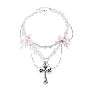 Dettaglio del ciondolo a croce e fiocco di raso rosa su collana di perle a strati