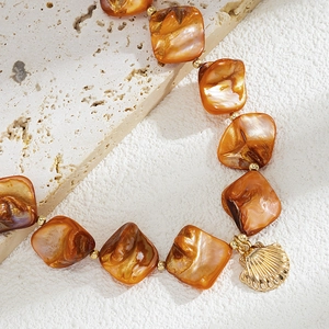 Dettaglio macro di perle in resina ambrata e ciondolo a conchiglia dorata su pietra