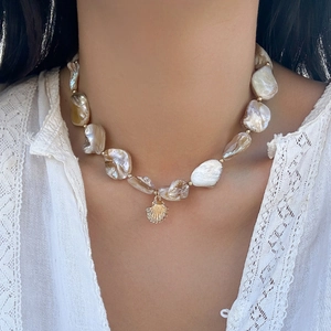 Dettaglio collana di perle barocche con ciondolo a conchiglia dorata su pizzo bianco