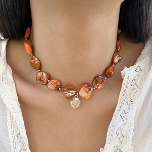 Dettaglio della collana di perline arancioni con ciondolo a conchiglia dorata raffinata
