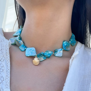 Primo piano della collana di conchiglie blu con ciondolo a conchiglia dorata su pizzo