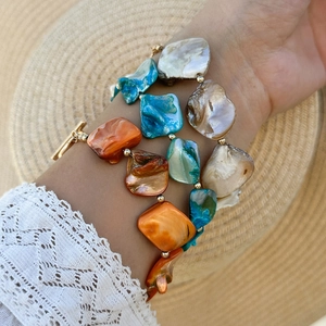 Dettaglio di un set di braccialetti boho con conchiglie colorate e chiusura oro