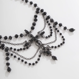 Detail of gothic black beaded necklace featuring faceted beads and dark metal cross pendant