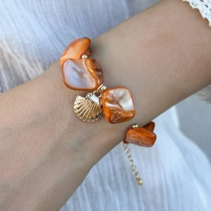 Dettaglio della collana con perle arancioni e un ciondolo a conchiglia dorata da mare