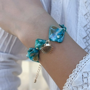 Dettaglio di un bracciale stile oceanico con pietre turchesi e ciondolo a conchiglia dorata