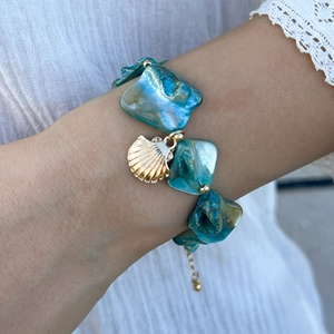 Dettaglio ravvicinato del bracciale di conchiglie blu cangianti con pendente dorato sul polso