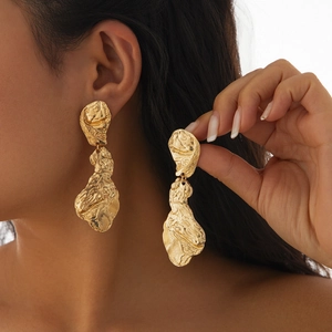 Gros plan de boucles d'oreilles pendantes dorées irrégulières au fini métal froissé