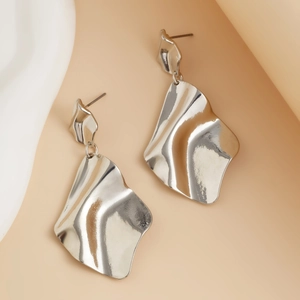 Détail montrant la texture métallique et la forme ondulée fluide des boucles d'oreilles