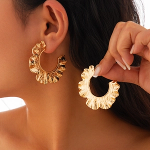Vue détaillée de grandes boucles d'oreilles dorées avec bords ondulés irréguliers