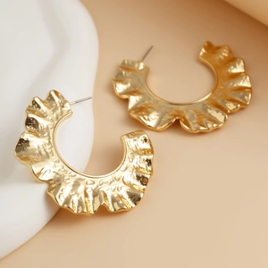 Détail macro de boucles d'oreilles dorées en C avec une texture métallique plissée