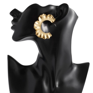 Détail de grandes boucles d'oreilles dorées en C avec texture métallique martelée