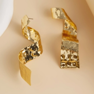 Gros plan détaillé de boucles d'oreilles torsadées en métal doré avec fini martelé