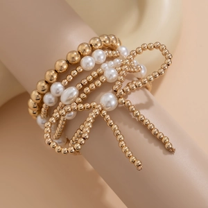 Primer plano de pulseras de perlas doradas en capas con un delicado detalle de lazo