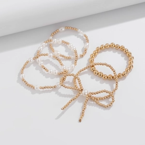 Detalle macro del elegante dije de lazo y pulseras de perlas en capas con acabado dorado
