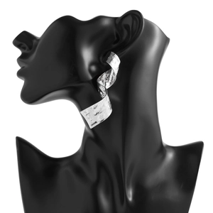 Détail des boucles d'oreilles spirales argentées avec texture en métal martelé sur support