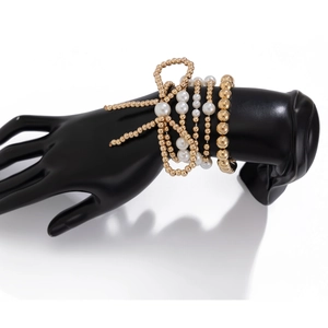 Primer plano de pulseras de cuentas apiladas con perlas blancas y doradas elegantes