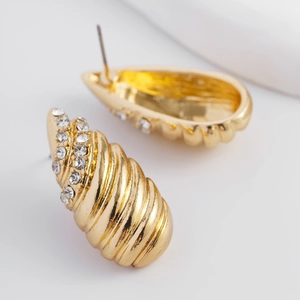 Détail macro de boucles d'oreilles spirales dorées ornées de strass blancs brillants