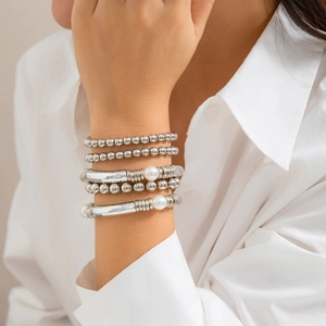 Detalle de las pulseras de cuentas plateadas con perlas y tubos de metal en la muñeca