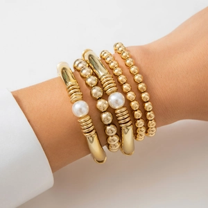 Detalle de conjunto de pulseras de cuentas doradas y brazaletes de perlas en la muñeca