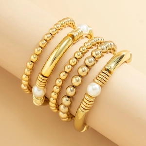 Detalle de un conjunto de pulseras doradas con perlas blancas y tubos metálicos curvos