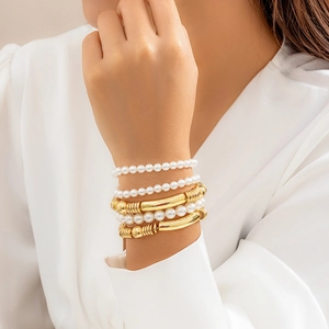 Detalle de un conjunto de pulseras con perlas blancas y cuentas de metal dorado en la muñeca