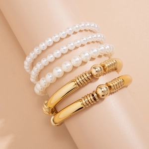 Detalle de set de 5 pulseras multicapa con perlas blancas y tubos de metal dorado
