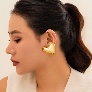 Close-up of a large gold liquid heart earring worn by a model on a beige background