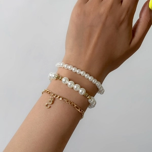 Vista detallada de pulseras de perlas en capas con colgante dorado en forma de S