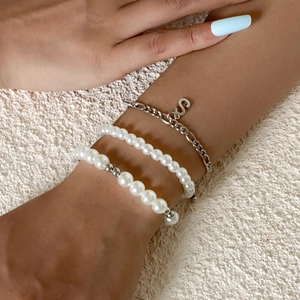 Primer plano de pulseras de perlas y cadena plateada con colgante de la letra S.
