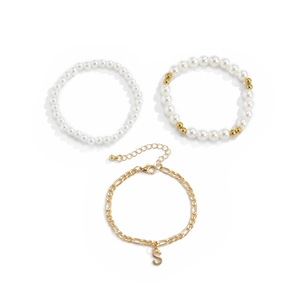 Detalle del juego de pulseras doradas con perlas y un colgante con la letra S