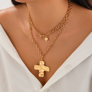 Detailopname van gouden gelaagde ketting met OT-sluiting, hart en gehamerde kruis hanger