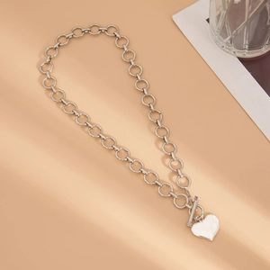 Zilveren punk ketting met hartvormige hanger en OT-sluiting op een beige achtergrond