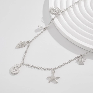 Detail of silver body chain featuring starfish, shell, and pearl charms for beach vacation