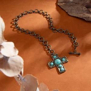 Detail van vintage punk kruisketting met groene turquoise stenen en OT-sluiting op hout