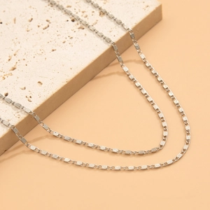 Detail of silver long tassel necklace with textured oval links on a beige stone stand