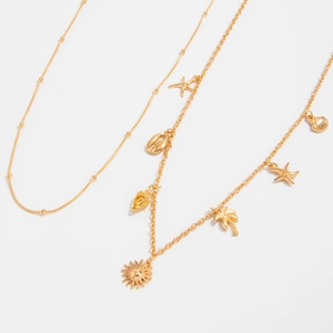 Close-up of golden body chain with starfish, palm tree, and shell charms on white surface