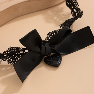 Détail d'un choker gothique en dentelle noire avec pendentif cœur et nœud en satin