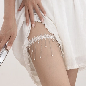 Détail d'une jarretière en dentelle blanche avec pampilles argentées et perles
