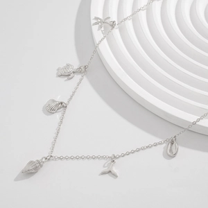 Detail of silver body chain featuring starfish, sea turtle, and shell charms on white background