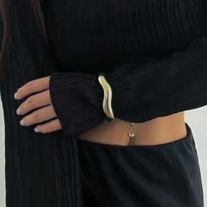 Macro shot of gold wavy cuff bracelet and double crystal navel piercing on model