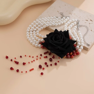 Detail of multi-layer pearl necklace featuring a black rose and red crystal tassel drips
