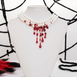 Macro detail of triple-layered pearl necklace with red crystal blood drip pendants